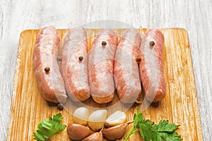 Sausages for frying, garlic, parsley on a wooden cutting board