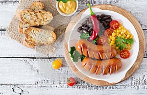 Sausages on the grill with vegetables on a platter. Top view