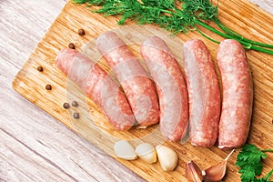 Sausages for grilling, dill and parsley and hot pepper on a wooden cutting board