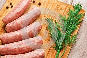 Sausages for grilling and dill on a wooden cutting board