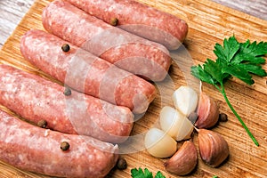 Sausages for grilling, garlic, parsley on a wooden cutting board
