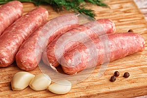 Sausages for grilling and garlic on a wooden cutting board