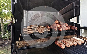 Sausages and hamburger patties have been cooked on the BBQ and are staying warm on the shelf while others cook