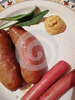 Sausages and hot dogs with mustard served on a plate and decorated with a few leaves arugula,top view from close up