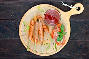 Sausages on skewers with ketchup and fresh tomatoes, served on a round wooden tray
