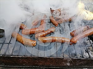 Sausages on a smoking grill, close-up. Sausage BBQ on wood ember, smoking. Barbecue, smoke background