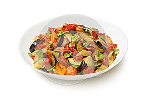 Sautéed eggplant zucchini carrots and tomatoes in a salad bowl isolated on white background.