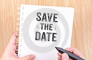 Save the date word on white ring binder notebook with hand holding pencil on wood table,Business concept