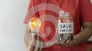 Save energy concept. Female hand holding a light bulb, coins in a jar with copy space