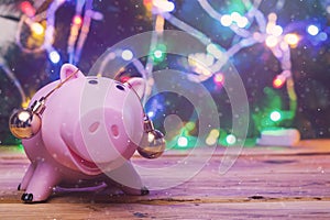 Save money for christmas. Piggy bank with xmas toys on ears against decorated with festive lights christmas tree. Christmas