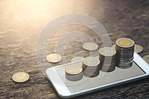 Save money concept with Coin stack growing on smartphone sunset background