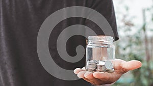 Save money concept, man hand holding a glass jar piggy bank with coins money, saving money growth for future finance accounting.