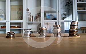 Save money concept. Stack of coins at home on a wooden table and a bookshelf in the background.