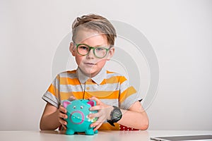 Save money. Kid hand putting coin into a piggy bank. Smart stylish child boy in yellow striped shirt and green glasses