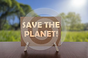 Save the planet! text on card on the table with sunny green park background. Ecology concept, recycle, reuse, reduce waste