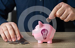 Save up for an idea. A man throws coins into a piggy bank with an idea light bulb symbol.