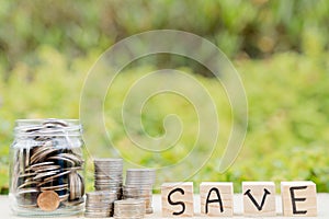 Save word on wooden block and jar full of coins on blurred green natural background. Saving money and investment concept