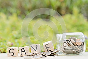 Save word on wooden block and jar full of coins on blurred green natural background. Saving money and investment concept