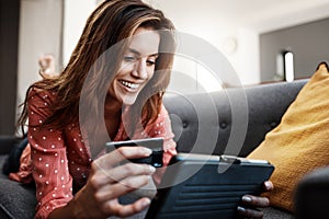 She saved so much shopping online. an attractive young woman using a digital tablet and credit card on the sofa at home.