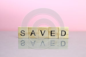 Saved word made of wooden letters on a pink background
