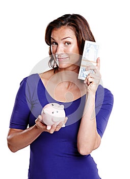 Saving dollars and cents. Studio portrait of a woman in her mid-30s smiling while holding a piggybank and a stack of