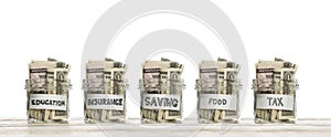Saving glass jars with us dollars money for education, insurance, food and tax on wooden board against white background