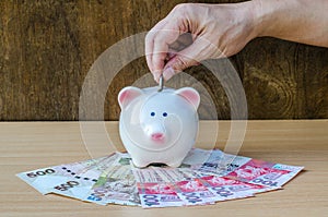 Saving, male hand putting a coin into piggy bank and money