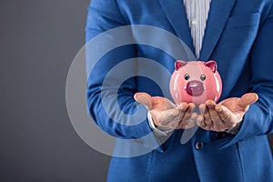 Saving money. Businesman holding pink piggy and putting coin into piggy bank