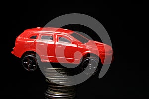 Saving money for a car. Banking, fast. Toy car and coins on black background. Miniature red car model on growing stack of coins.