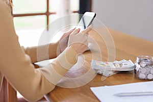 Saving money concept, Asian woman use smartphone and reading data after count the amount of savings