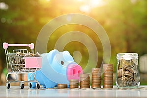 Saving money concept with Coin stack growing, Cart, Bottle and piggy bank business on sunset background