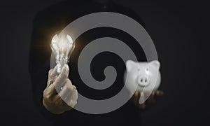 Saving money concept. Man holding light bulb and piggy bank on black background