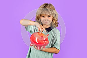 Saving money concept. Portrait of a little boy putting money on a moneybox. Child saving money in a piggybank on studio