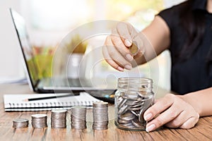 Saving money and finances concept, Close up hand woman hand put coins in jug glass with Calculate with calculator