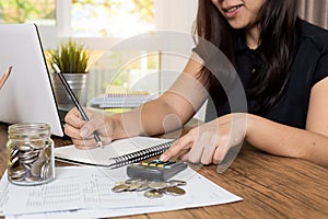 Saving money and finances concept, Close up hand woman hand put coins in jug glass with Calculate with a calculator