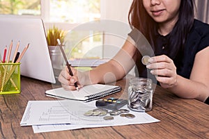Saving money and finances concept, Close up hand woman hand put coins in jug glass with Calculate with a calculator