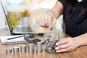 Saving money and finances concept, hand woman hand put coins in jug glass with Calculate with a calculator