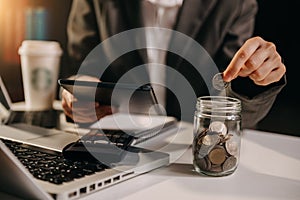 Saving money with hand putting coins in jug glass and calculator to calculate budget concept finance and accounting