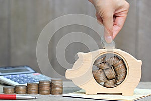 Saving money for prepare in future concept, Woman hand putting a coin into piggy bank wood on wooder background