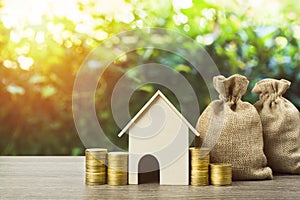 Saving money or property investment or buy a new home concept. A small house model with stack of coins and money bag on wood table