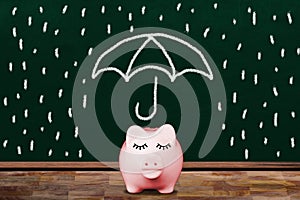 Saving For a Rainy Day Concept With Piggy Bank Shielded From Rain