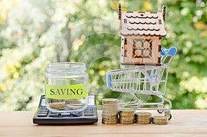 `Saving` text label on the jar. savings, donation, financial, future investment concept. wooden house and shopping cart