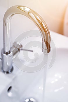 Saving water: Close up of spigot with clear, flowing water. Morning sun