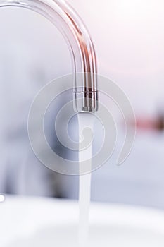 Saving water: Close up of spigot with clear, flowing water. Morning sun