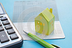 Savings account passbook, calculator, pen and yellow paper house on blue background photo