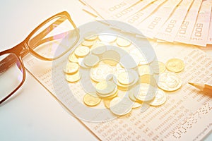 Savings account passbook, Thai money, coins, eye glasses and pencil on blue background