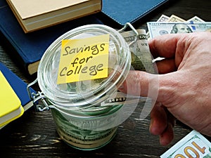 Savings for college. Hand puts money in a glass jar.