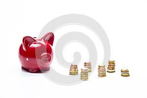 Savings and Finances Concepts. Red Piggy Moneybox Along With Plenty Coins Stacks. Isolated on White Background