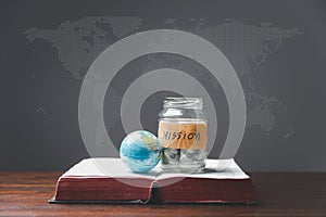 Savings jars full of money and globe with Holy Bible for mission, Mission christian idea. bible and book on wooden table,