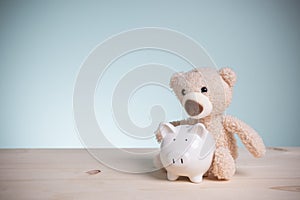 Savings money to buy a home for the future. Little brown teddy bears with piggy banks on an old wooden table with copy space.